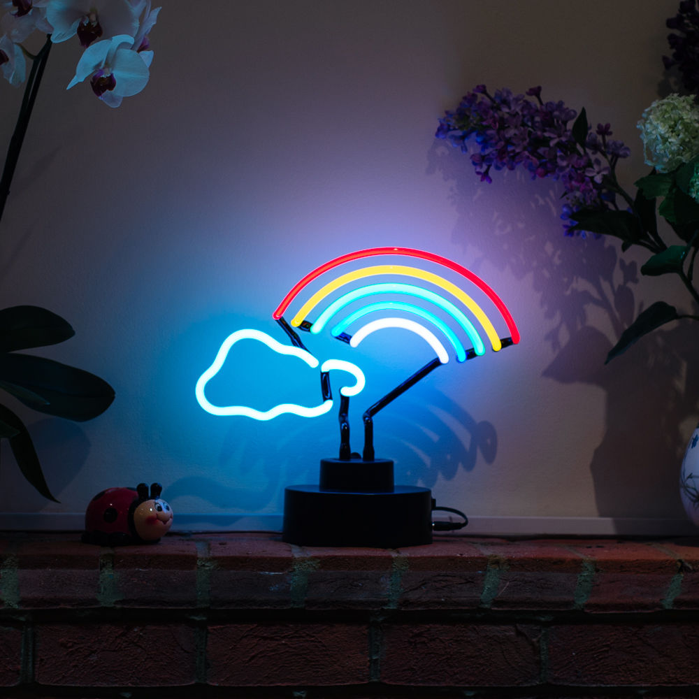 A handcrafted glass rainbow cloud table neon sign glowing brightly with visible wiring and a sturdy base on a wooden surface.