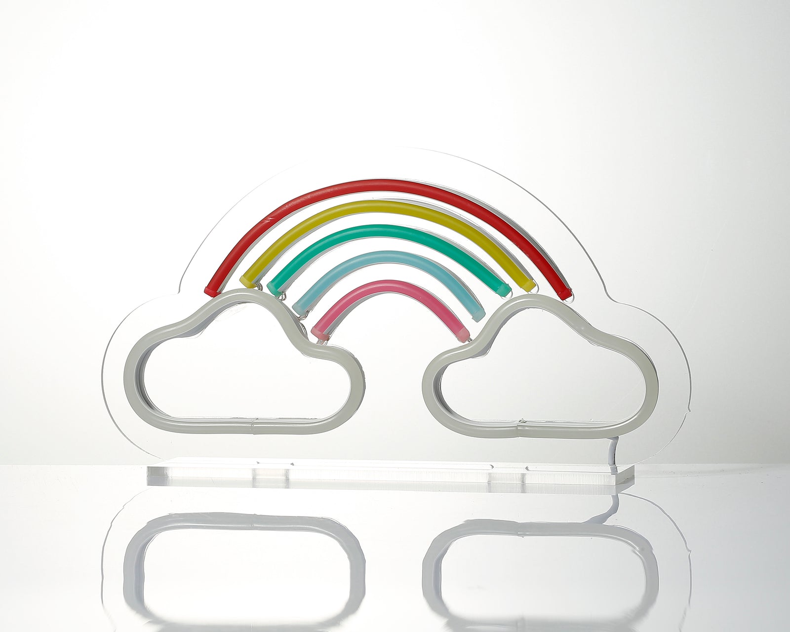Close-up of the lit 'Rainbow' desk neon sign showing distinct colored tubes glowing against the acrylic backing, set up on a surface with natural reflections.