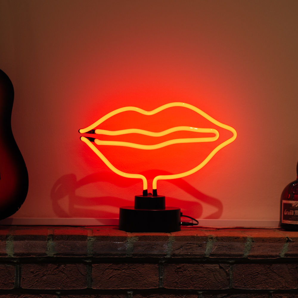 p: Real-product photo of a neon sign depicting bright red lips. It is glowing vibrantly on its black cylindrical table stand.