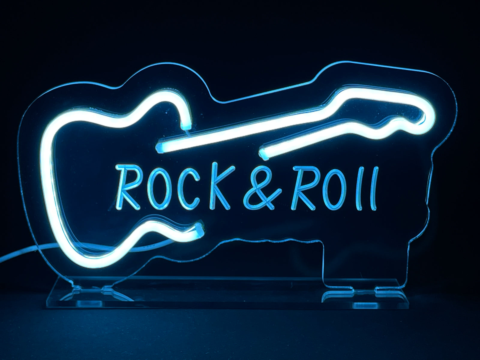 Front-facing view of the illuminated blue, red, and white "Rock Roll" neon desk sign with its clear acrylic stand against a plain background.