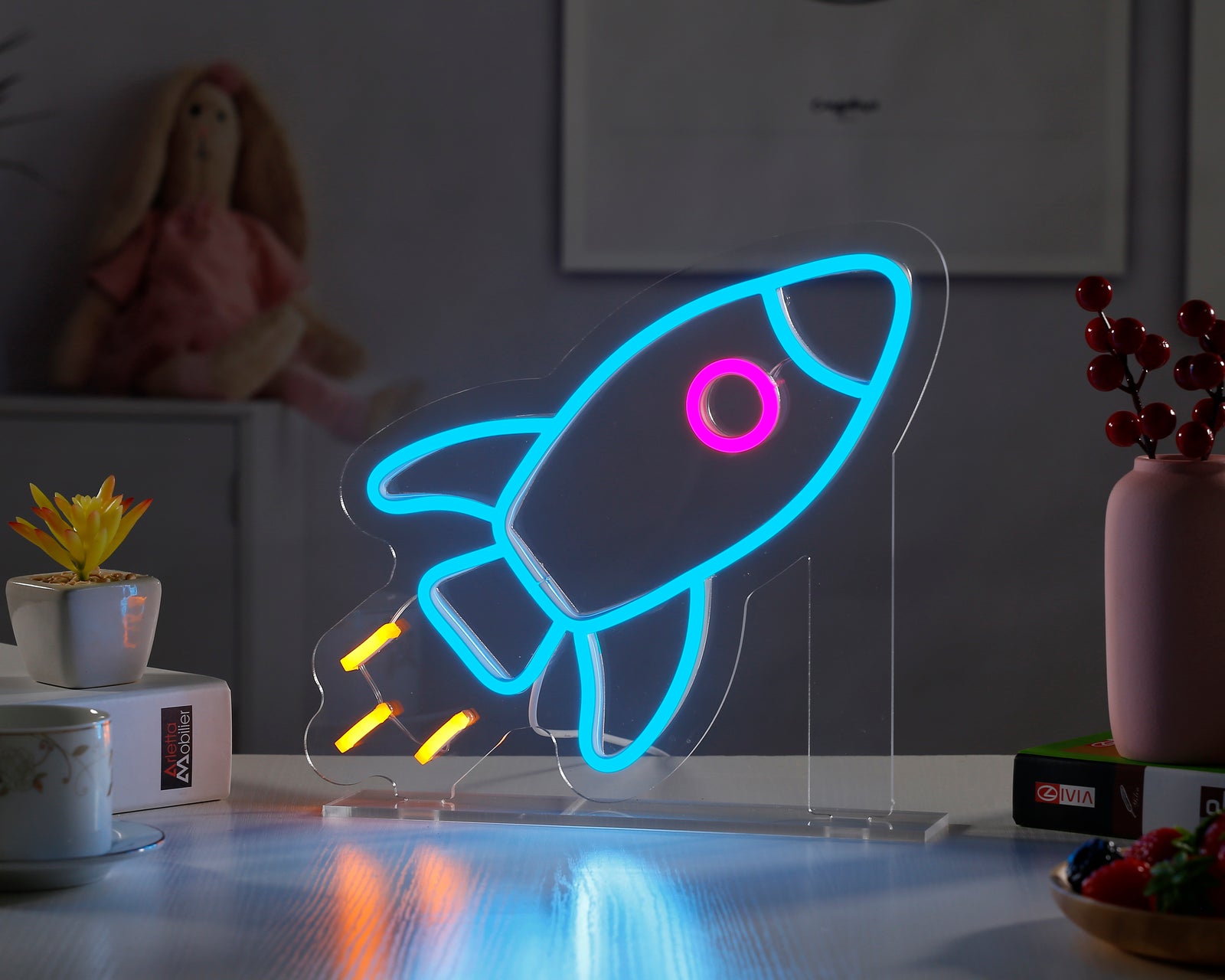 Rocket Desk Neon Sign glowing blue on a wooden desk next to a plant