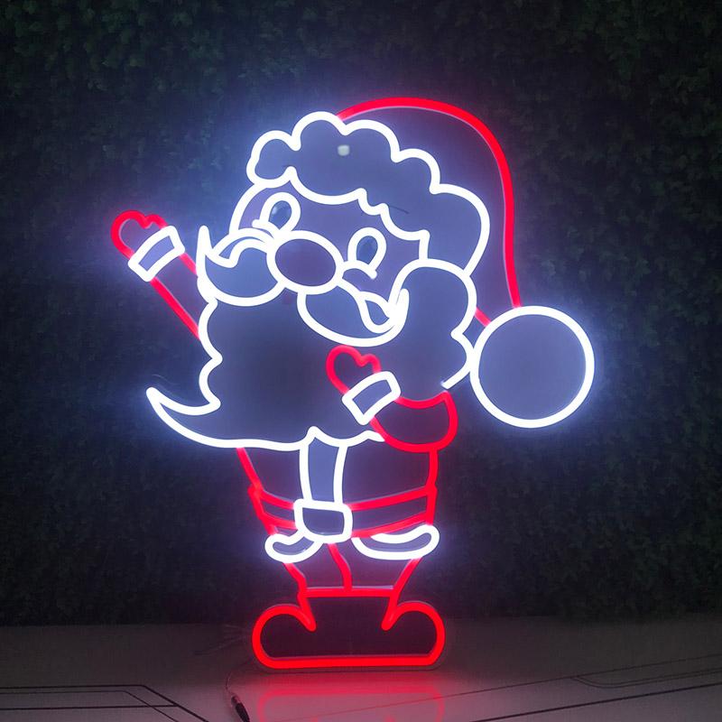 A bright red Santa Claus head neon sign illuminated in a cozy, dark room. The sign features the classic profile of Santa with his beard and hat, glowing with a festive red light on a dark wall.