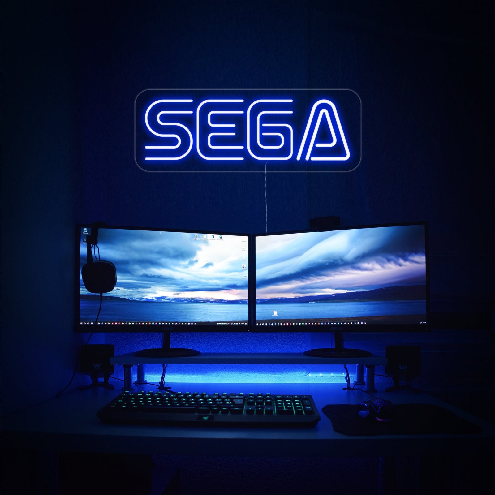 A radiant blue neon sign displaying the classic SEGA logo, mounted on a clear backing on a dark background.