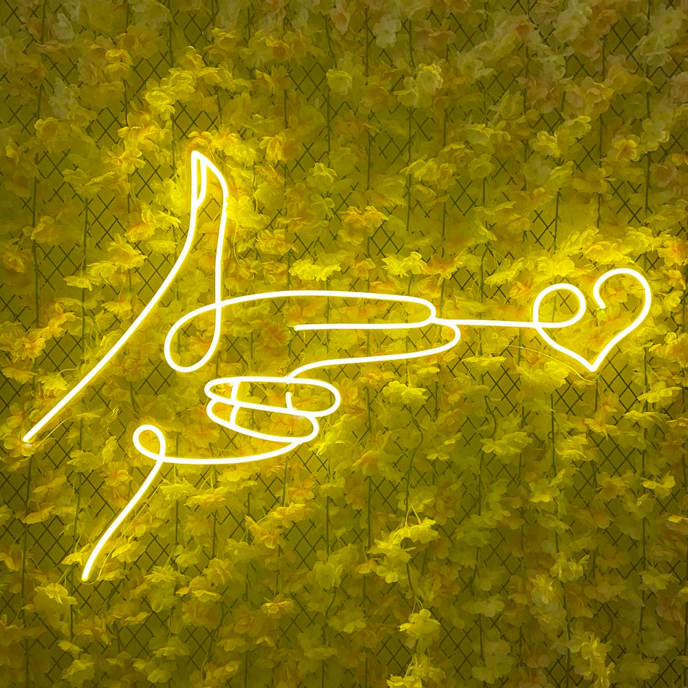 Detailed view of the 'Shoot Love Heart' neon sign illuminating against a vibrant yellow flower wall, highlighting fabrication details.