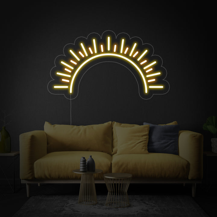 A glowing yellow "Sun Sunset" artistic neon sign on a clear backboard against a neutral wall, illuminated.