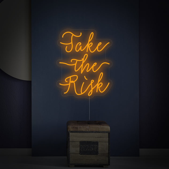A focused photo of the 'Take The Risk' neon sign, showing the clear acrylic backing and glowing letters.