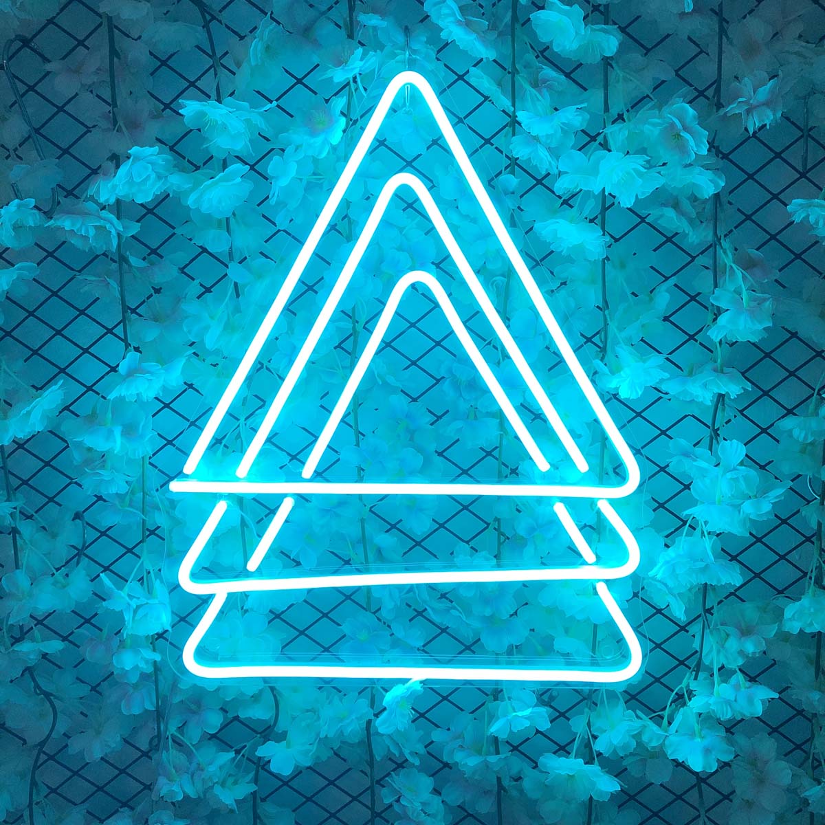 Three triangle geometric neon sign glowing with colorful light on a decorated grid wall background.