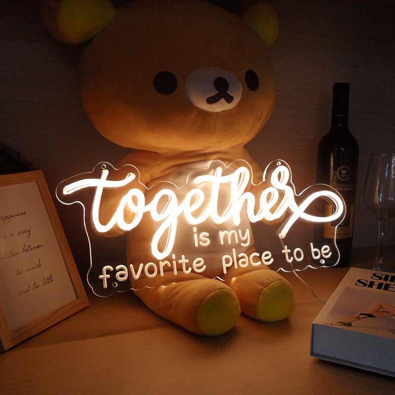 Small white neon sign spelling out 'Together Is My Favorite Place To Be' illuminated on a textured beige wall with natural light.