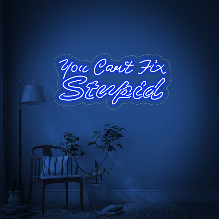 A clean product photograph of the 'You Can't Fix Stupid' neon sign, featuring bright orange text tubes mounted on a transparent acrylic backing cut to shape, glowing brightly against a dark, textured brick wall.