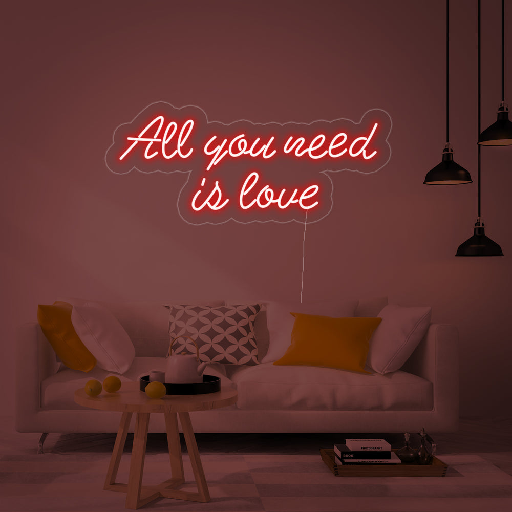 Close-up of the lit 'All You Need is Love' neon sign showing the distinct glowing tubes and backing plate.