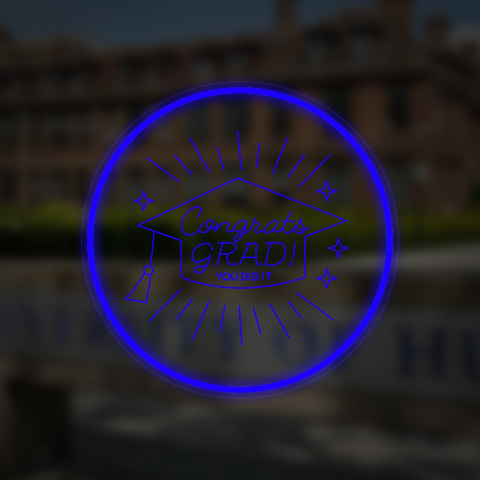 Small 'Congrats Grad' neon sign illuminated over a blurred university building background.