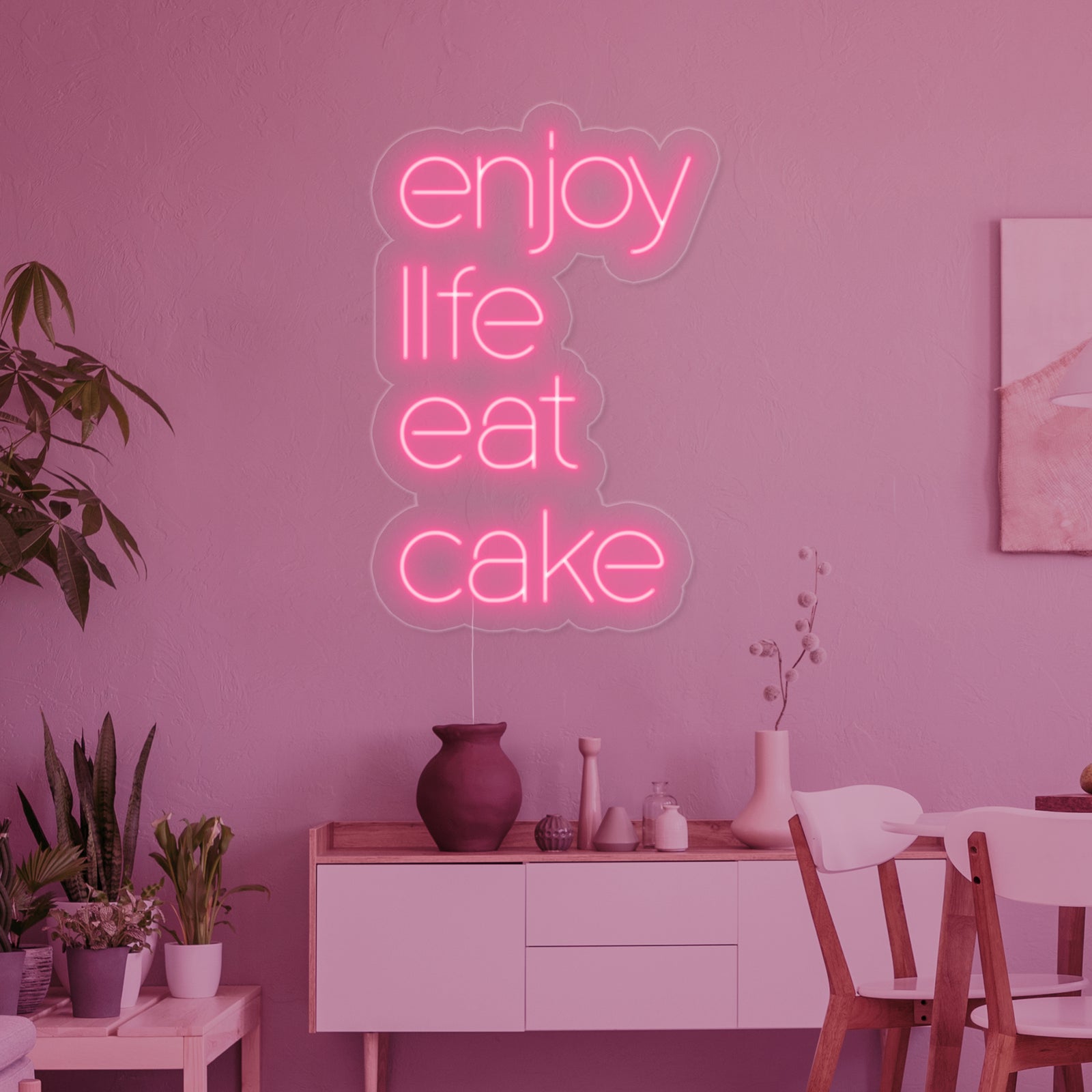 A glowing 'Enjoy Life Eat Cake' neon sign with clear script lettering and stylized accents.
