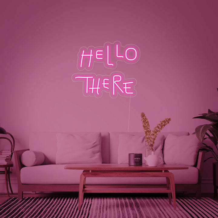 A lifestyle shot showing the glowing "Hello There" neon sign mounted above a sofa in a contemporary, warm-lit apartment.