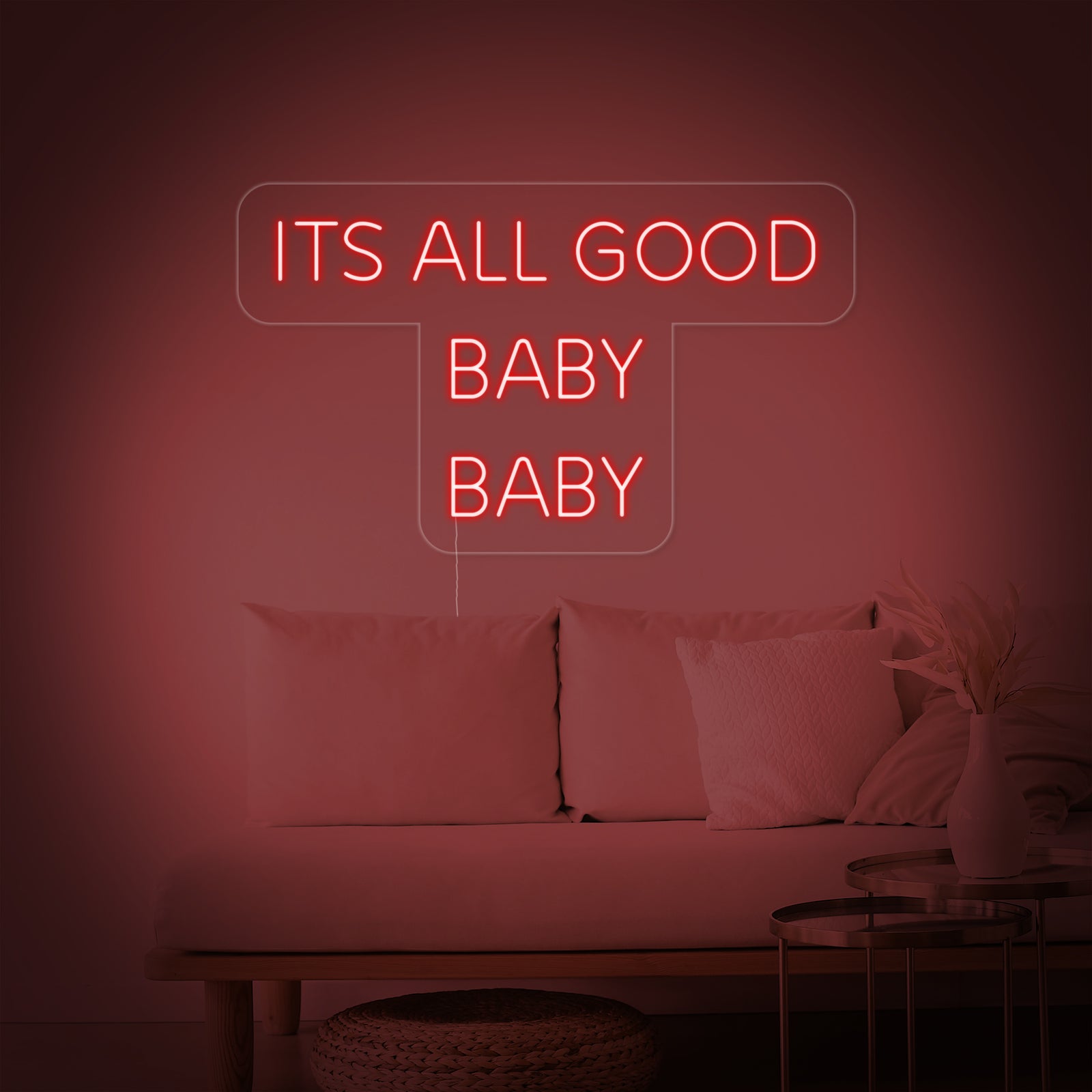 A close-up view of the glowing 'It's All Good Baby Baby' neon sign against a dark textured wall, showing its vibrant color and craftsmanship.